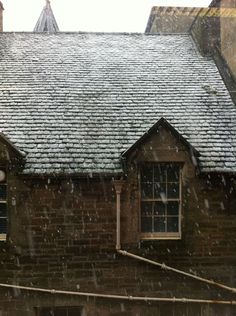 an old brick building with snow falling on the roof