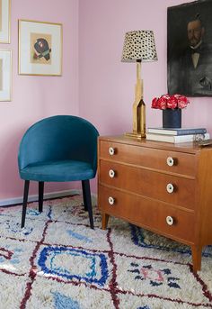 a blue chair sitting next to a dresser in a room with pictures on the wall