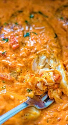 a spoon with some food in it on top of a pan filled with cheese and sauce