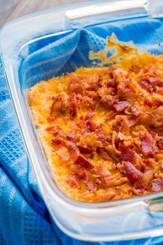 a casserole dish with bacon and cheese in it on a blue cloth next to a spoon