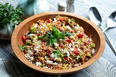 a wooden bowl filled with rice and vegetables on top of a table next to utensils