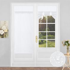 an open door with white curtains and flowers on the side table in front of it