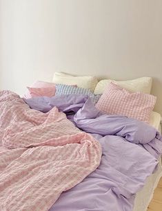 an unmade bed with pink and purple sheets on it in a white walled room