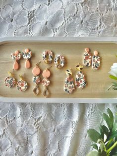 several pairs of earrings are on a tray next to a potted plant and white lace