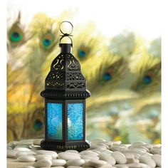 a blue lantern sitting on top of a table next to white rocks and peacock feathers