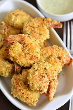 some fried food on a white plate next to a bowl of ranch dressing and a fork