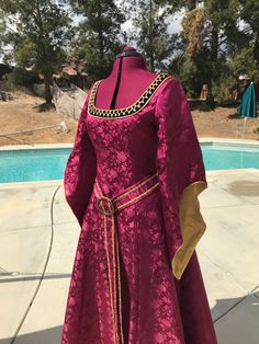 a woman's pink dress with gold trim around the waist and sleeves next to a swimming pool