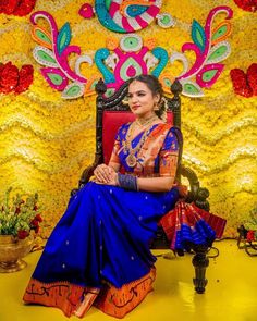 a woman is sitting on a chair in front of a wall with flowers and decorations