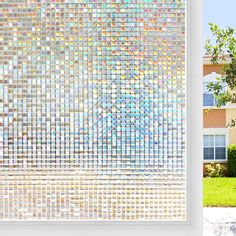 a window covered in multicolored glass next to a tree and building with grass