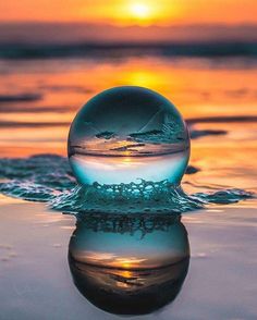 a glass ball sitting on top of the water at sunset, reflecting the sun in the distance