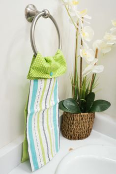 a towel rack with a green bow on it next to a white sink and potted plant