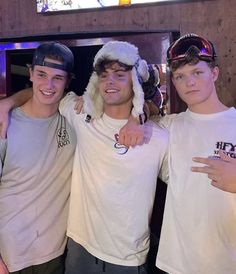 three young men standing next to each other wearing white t - shirts and santa hats