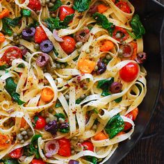 a pan filled with pasta and vegetables on top of a wooden table