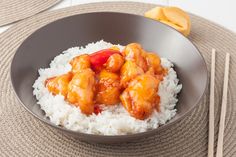 a bowl filled with rice and chicken on top of a table next to chopsticks