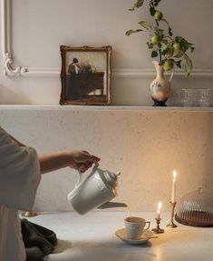 a woman pouring tea into a cup on top of a table next to a lit candle