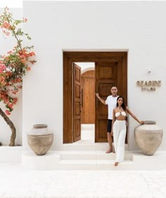 a man and woman standing in front of a door with vases on either side