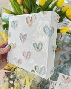 a person holding up a box with hearts on it and some flowers in the background