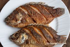 two fish on a white plate sitting on a wooden table