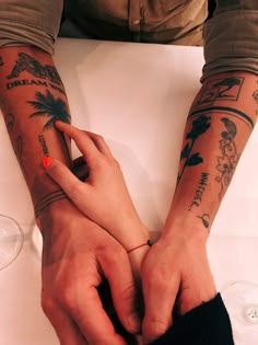 two people sitting at a table with tattoos on their arms and hands, one holding the other's hand