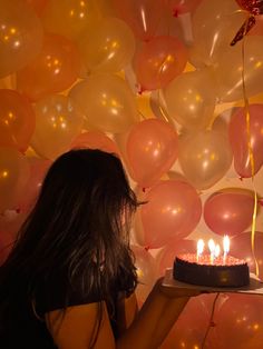 a woman holding a cake with candles in front of balloons