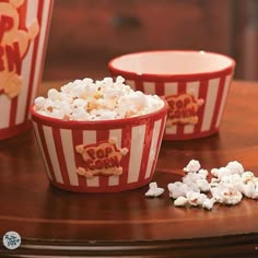 three red and white striped bowls filled with popcorn on top of a wooden table next to each other