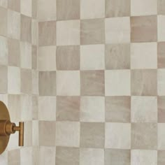 a white and beige tiled wall with a gold faucet next to it's hand held shower head