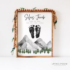 a wooden frame with a baby's footprints and pine trees in the mountains on it