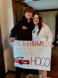 a man and woman standing next to each other holding a sign that says life is a highway