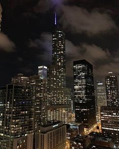 the city skyline is lit up at night with skyscrapers in the foreground and clouds in the background