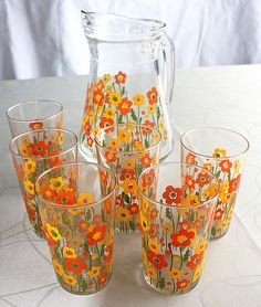 a glass pitcher and six glasses with flowers painted on the inside are sitting on a table