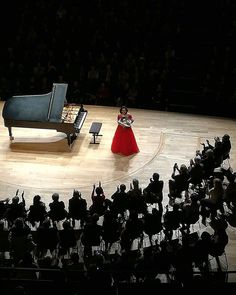 a woman in a red dress standing next to a grand piano on top of a stage