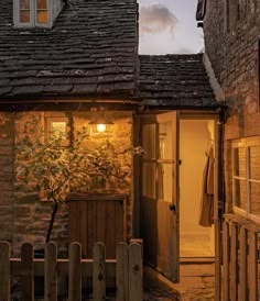 an old stone building with a potted plant in the doorway at night, next to a wooden fence