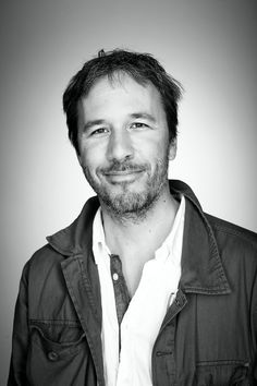 a man wearing a green jacket and white shirt smiles at the camera while standing in front of a gray background