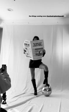 a woman is reading a newspaper while sitting on a soccer ball in front of her