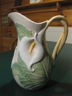 a white flower vase sitting on top of a green table next to a wooden shelf