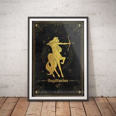 zodiac sign sagitrat framed in black and gold on a wooden floor next to a brick wall