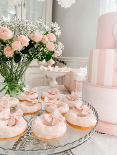 a table topped with pink frosted donuts next to a vase filled with flowers