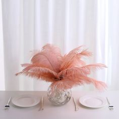 there is a vase with some pink feathers on it and silverware next to the plate