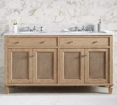 a bathroom vanity with two sinks and wicker doors on the front, against a white marble wall