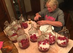 a woman sitting at a table filled with lots of bottles and jars full of liquid