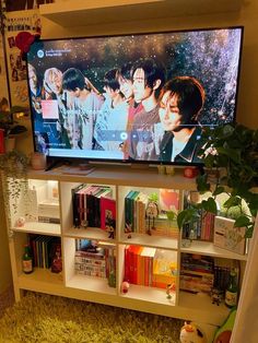 a flat screen tv sitting on top of a white book shelf next to a plant