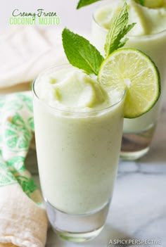 two glasses filled with lemonade and mint on top of a white tablecloth next to other glassware