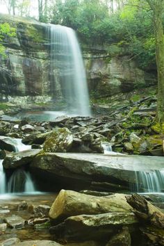 a waterfall in the woods with rocks and trees