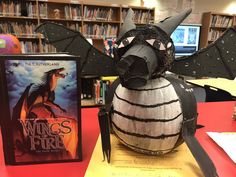 a paper mache dragon sitting on top of a table next to a paperback book