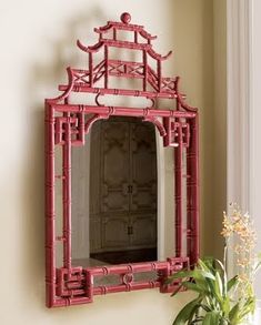 an image of a red bamboo mirror on the wall in front of a vase with flowers