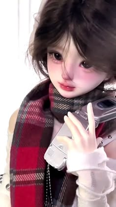 a doll holding a cell phone up to her face and wearing a scarf around her neck