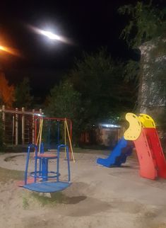 an empty playground at night with the moon in the sky above it and children's play equipment