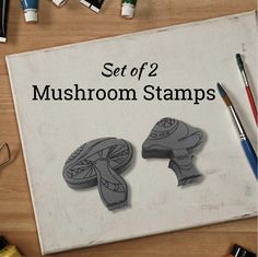 a set of 2 mushroom stamps sitting on top of a wooden table next to markers and pens