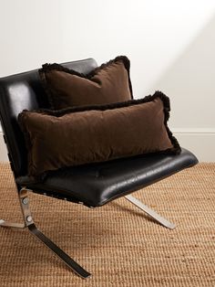 two brown pillows sitting on top of a black chair next to a white wall and carpet