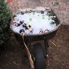 an old wheelbarrow filled with beer bottles and ice in the yard next to a brick wall